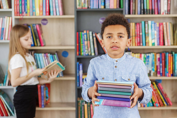 Озил учится, возвращается в школу и образование. Детский школьник читает книги в библиотеке или книжном магазине. Всемирный день книги - Фото, изображение