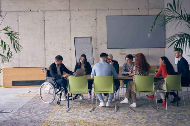 A diverse group of business professionals, including an person with a disability, gathered at a modern office for a productive and inclusive meeting - Photo, image