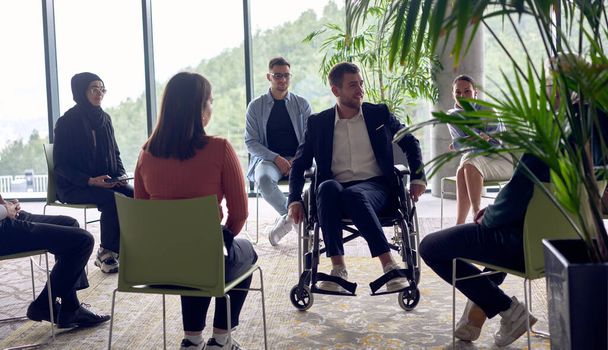 A businessman in a wheelchair in the center of the circle, passionately sharing his business ideas with his colleagues, fostering an atmosphere of collaboration and innovation in a dynamic and - Fotografie, Obrázek