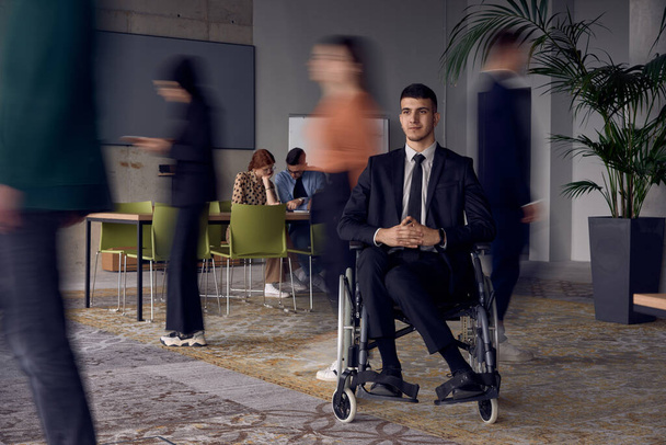 A businessman in a wheelchair in a modern office, surrounded by his colleagues who are portrayed with blurred movements, symbolizing their support and solidarity as they navigate the workspace - Zdjęcie, obraz