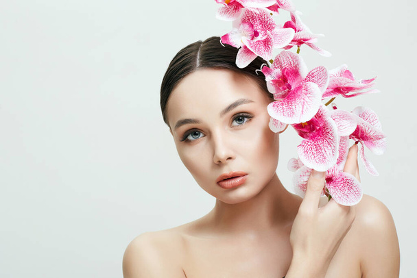 Gyönyörű nő és virágok. Szépség portré lány orchideavirággal. Tiszta bőr arc, gondozás - Fotó, kép