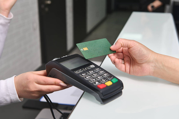 NFC teknolojisi ile kredi kartıyla ödeme yapan tanınmayan kadın müşteriyi kapatın. Klinikteki resepsiyon masasında POS terminal okuyucusunun üzerinde plastik bir banka kartı bulundurun. - İnsanlar. İş için. Finans - Fotoğraf, Görsel