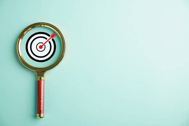 The magnifier glass highlights a target board, emphasizing the business objective, target search concept, and success. Isolated on a background with copy space. - Foto, Imagen