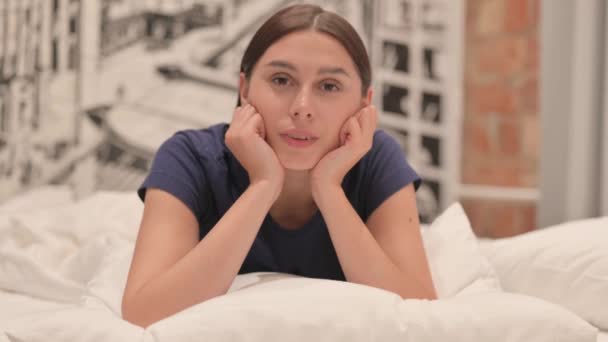 Komoly fiatal Latina nő fekszik az ágyban a hason Nézi a kamera - Felvétel, videó