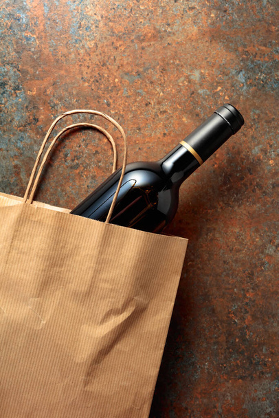 錆びた金属の背景に赤ワインのボトル入りの紙のショッピングバッグ。トップビュー、コピースペース. - 写真・画像
