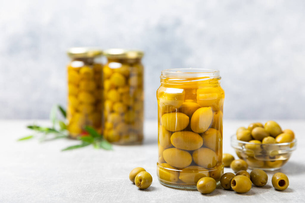 Olives in a glass jar on a concrete background. pitted green olives in jar.Pickled olives in glass jar. On a wooden background.Marinaded olives. Space for text.Space for copy. Vegan food. - Foto, afbeelding