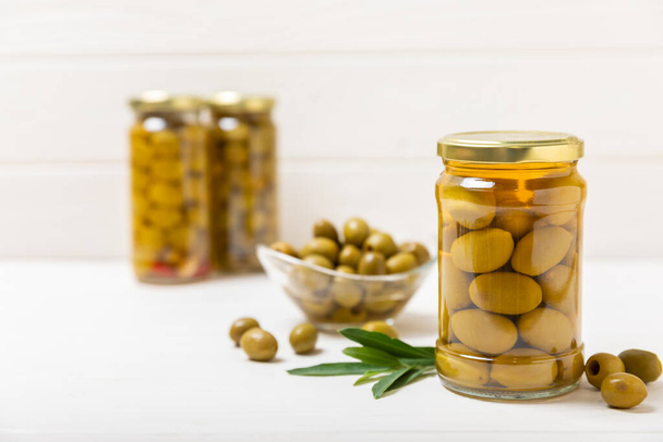 Olives in a glass jar on a white wooden background. pitted green olives in jar.Pickled olives in glass jar. On a wooden background.Marinaded olives. Space for text.Space for copy. Vegan food. - Foto, afbeelding