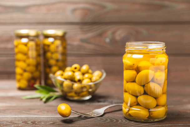 Olives in a glass jar on a brown wooden background. pitted green olives in jar.Pickled olives in glass jar. On a wooden background.Marinaded olives. Space for text.Space for copy. Vegan food. - Foto, afbeelding