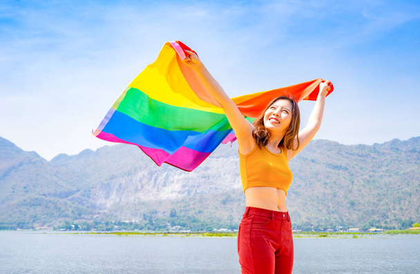 jeune asiatique femelle tenant lgbt coloré arc-en-ciel drapeau plus, fond bleu ciel, heureux lesbienne femme agitant lgbtq gay drapeau soutien ou le respect de la diversité des genres, homosexuel, bisexuel, transsexuel, queer - Photo, image