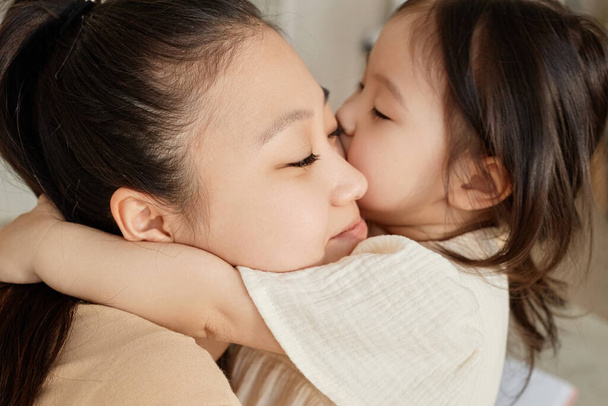 Азиатская маленькая девочка обнимает и целует свою маму - Фото, изображение