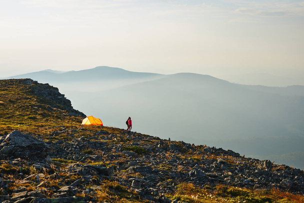 People spending summer vacation in mountains, standing by tent looking at sunrise over valley. Active couple hiking in mountains. Yellow tent put over valley. Foggy mountain landscape view at sunrise - Foto, afbeelding