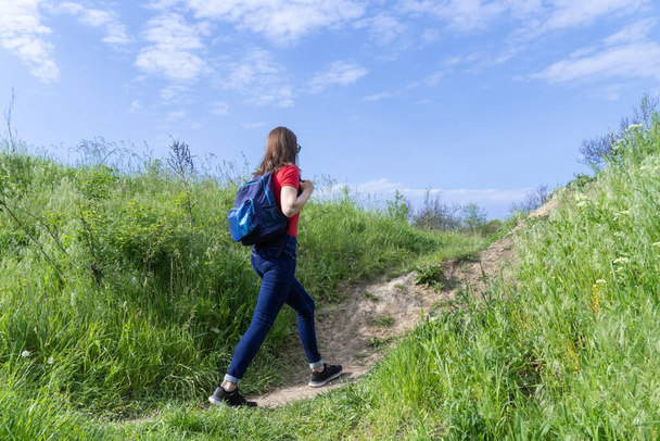 Tourist woman with backpack walking in deciduous forest. Active adult leisure of hiking in green valley. Person enjoy wanderlust and view of the spring grassy hill. Female hiker explore of wildlife. - Fotoğraf, Görsel