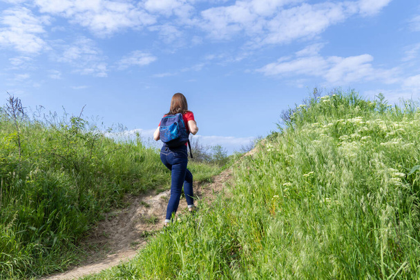 Turista nő hátizsákkal sétál a lombhullató erdőben. Aktív felnőtt szabadidős túrázás zöld völgyben. Az ember élvezze a vándorlást és a tavaszi füves dombra való kilátást. Női túrázó felfedezni vadon élő állatok. - Fotó, kép