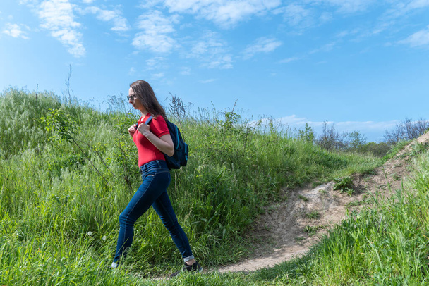 Tourist woman with backpack walking in deciduous forest. Active adult leisure of hiking in green valley. Person enjoy wanderlust and view of the spring grassy hill. Female hiker explore of wildlife. - Photo, image