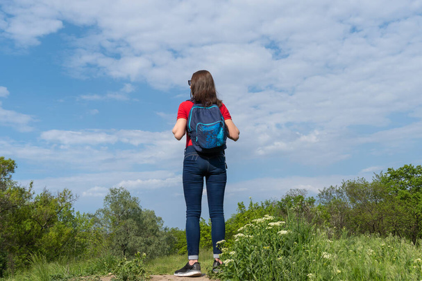 Tourist woman stand on edge and look on deciduous forest. Active adult leisure of hiking in green valley. Person enjoy wanderlust and view of the spring grassy hill. Female hiker explore of wildlife. - Photo, Image