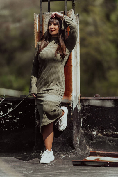 A confident and stylish plus-size woman walking by a modern building in an olive green dress, radiating beauty, empowerment, and self-love - Photo, Image