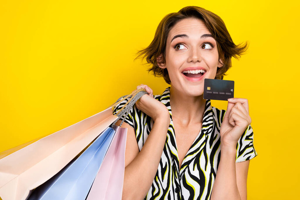 Portrait of excited charming woman wear striped blouse look empty space hold card shopping bags isolated on yellow color background. - Foto, Bild