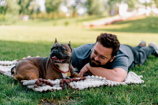 bärtiger Mann ruht im Park mit seinem Hund Französisch Bulldogge im Freien liegend auf Laken Sommer Picknick - Foto, Bild
