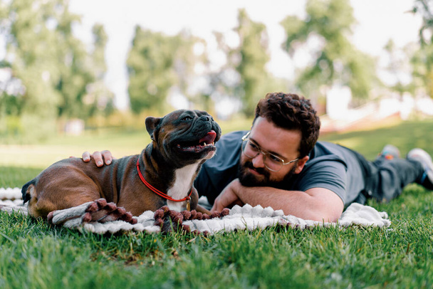 bärtiger Mann ruht im Park mit seinem Hund Französisch Bulldogge im Freien liegend auf Laken Sommer Picknick - Foto, Bild