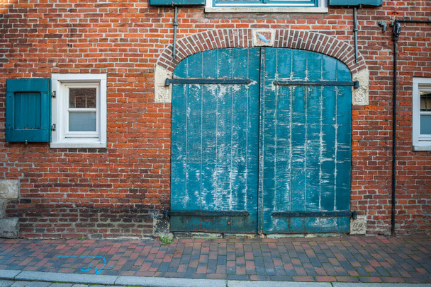 Vooraanzicht op een oude bakstenen gevel met een gesloten poort en kleine ramen aan beide zijden. - Foto, afbeelding
