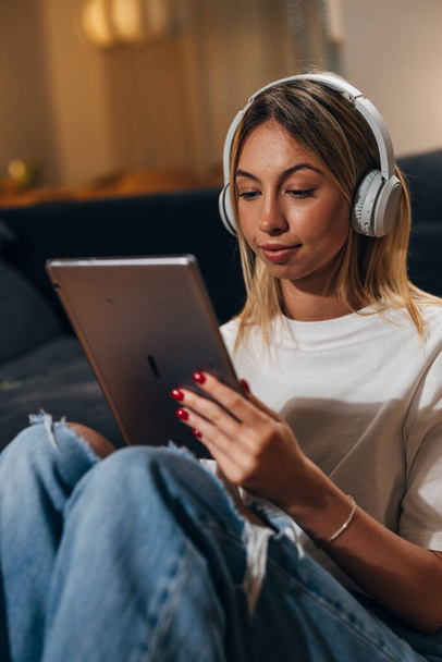 Blonde woman watching something on tablet with headphones. - 写真・画像