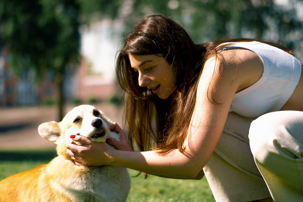 retrato de una joven y un lindo perro corgi, el propietario besa al perro en la nariz en un paseo por el parque - Foto, imagen