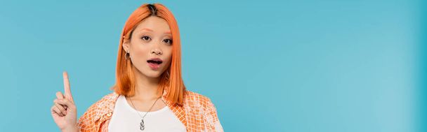 pointing with finger, amazed face, young asian woman with dyed hair showing something on camera on blue background, generation z, casual attire, young culture, expressive, website banner  - Photo, Image
