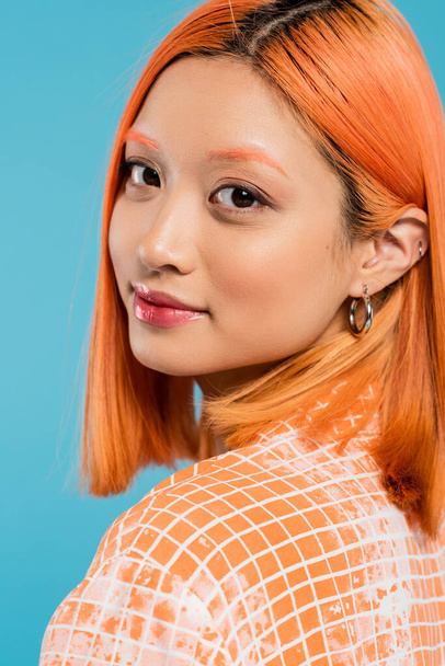 portrait of young asian woman with natural makeup, lip gloss, hoop earrings and short dyed hair looking at camera on blue background, youth, generation z, fashion, casual attire - Foto, Bild