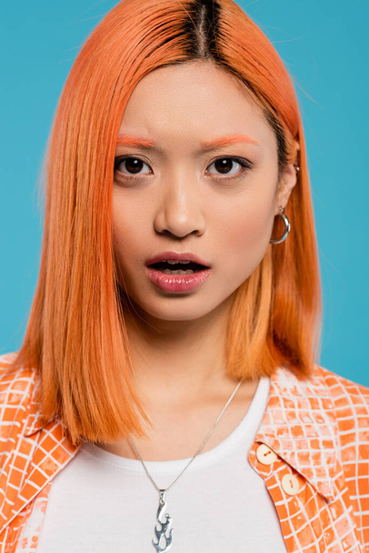 shocked face, young asian woman with red hair looking at camera and standing with open mouth on blue background, casual wear, generation z, emotional, wow, surprised, astonished  - Foto, Imagem