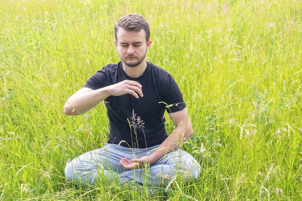 Meditasyon yapan genç adam. Doğada ahenk bulmak. Huzur arayan bir adam - Fotoğraf, Görsel