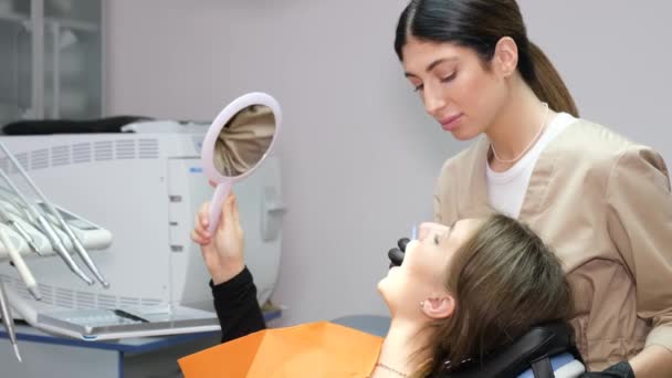 歯科治療中の歯科医と患者.患者は快適な歯科用椅子に座り、歯科用鏡を調べる。現代歯科におけるペンス歯科治療 - 映像、動画