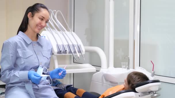 Aangename, lachende vrouwelijke tandarts tijdens een tandheelkundig consult met een kleine jongen. Kindertandheelkunde. Tandheelkundige behandeling bij kinderen. - Video