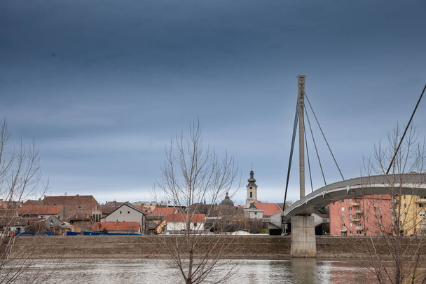 Sremska Mitrovica 'lı Panorama ve Saint Irinej köprüsü (En Çok Svetog Irineja) soğuk bir kış öğleden sonrasında. Sremska Mitrovica, Sırbistan 'ın kuzeyindeki Srem Bölgesi' nin önde gelen kentlerinden biri.. - Fotoğraf, Görsel
