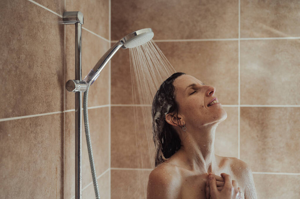 若い女性は長い一日の後に熱いシャワーを楽しんでいます。彼女のシャンプーされた髪の毛で走る水. - 写真・画像