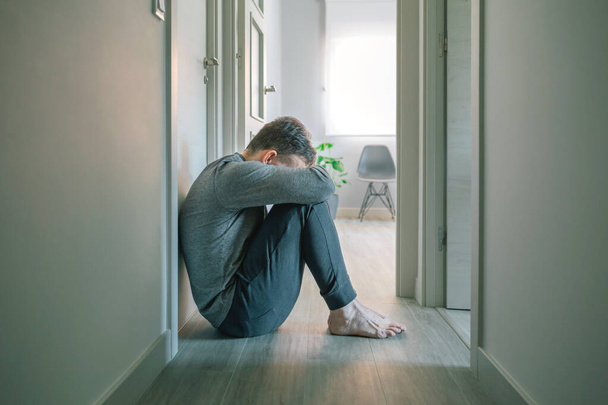 Unerkennbarer Mann im Schlafanzug mit psychischen Störungen und Selbstmordgedanken weinend auf dem Boden eines psychiatrischen Zentrums sitzend - Foto, Bild
