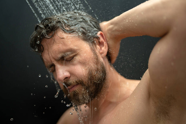 Millennial man washing hair in bath. Guy bathing shower head in bathtub. Face in foam in shower. Bathing man taking shower. Closeup guy showering. Shower concept. Man is under water drops in showers - Photo, image