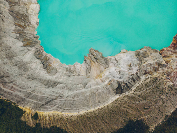 Top aerial view of turquoise sulfur water lake, surrounded by rock cliff at Kawah Ijen volcano in East Java, Indonesia. - Photo, Image