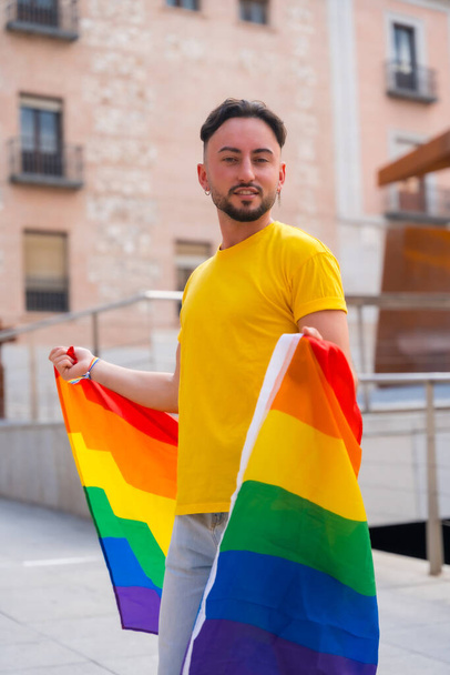 Portrait of attractive gay man smiling with rainbow lgbt flag in the city, pride and homosexual party - Foto, Bild