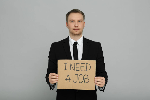 Unemployed man holding sign with phrase I Need A Job on light grey background - Fotografie, Obrázek