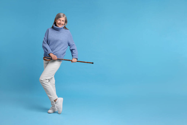 Senior woman with walking cane on light blue background, space for text - Φωτογραφία, εικόνα