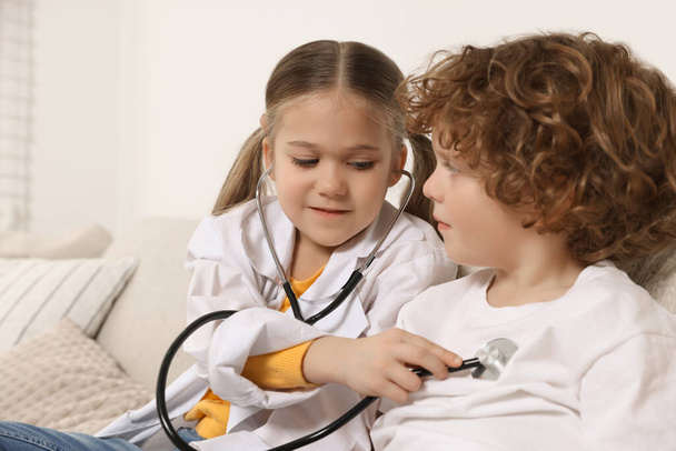 Little girl playing doctor with her friend at home - Фото, изображение