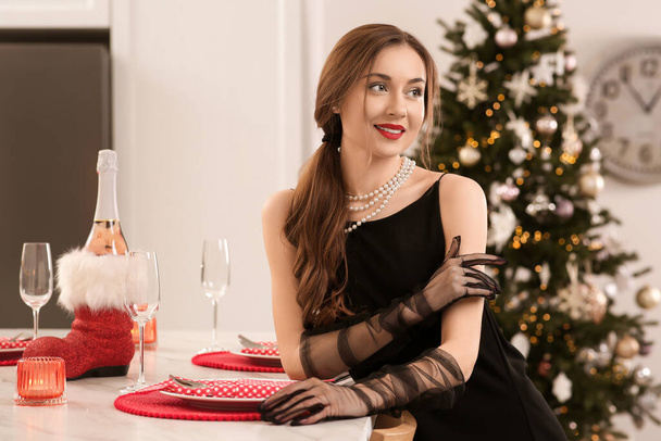 Beautiful young woman near Christmas tree and table in kitchen - Foto, Imagem