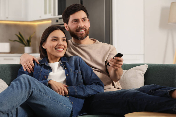 Happy couple watching TV on sofa at home - Valokuva, kuva