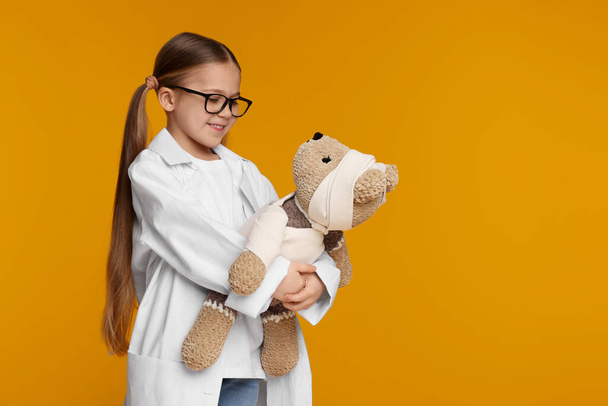 Little girl in medical uniform with toy bear on yellow background. Space for text - Foto, Bild