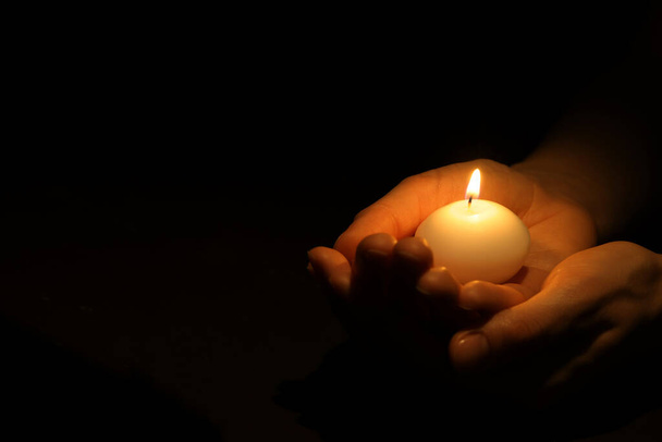 Woman holding burning candle in hands on black background, closeup. Space for text - Valokuva, kuva