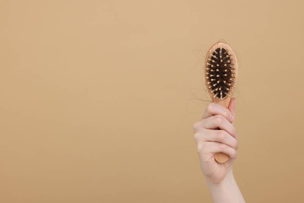 Woman holding brush with lost hair on beige background, closeup and space for text. Alopecia problem - Foto, immagini