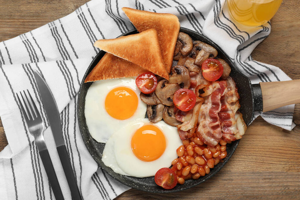 Serving pan with fried eggs, mushrooms, beans, bacon, tomatoes and toasted bread on wooden table, flat lay. Traditional English breakfast - Foto, Imagem