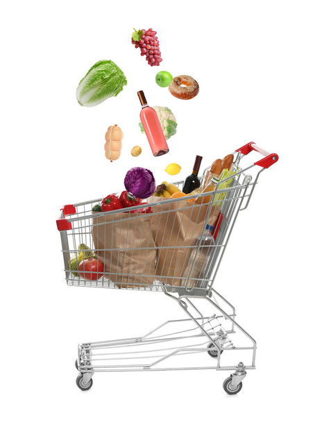 Market assortment. Different products falling into shopping cart on white background - Foto, Bild