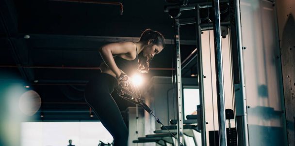 Спортивная женщина упражняется на мультистанцию в тренажерном зале для мышц рук и плеч. Тренажерный зал. - Фото, изображение