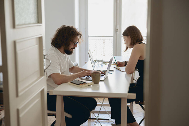 Mężczyzna i kobieta pracują przy stole w salonie w domu. Koncepcja pracy na odległość - Zdjęcie, obraz